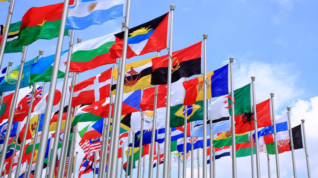 Flagpoles with flags of nations from around the world waving in the breeze under a blue sky